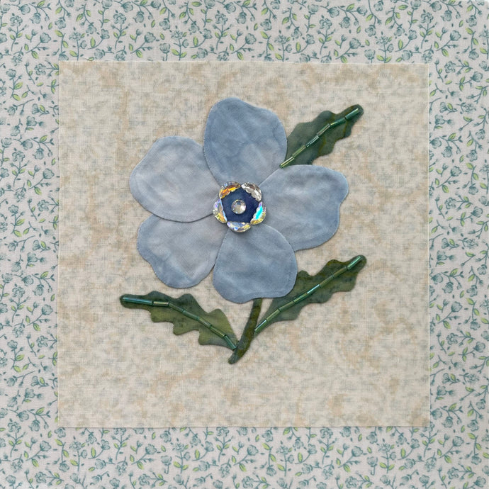 8 x 8 fabric collage artwork featuring a soft blue flower with crystal center and green stitched leaves made from inherited textiles