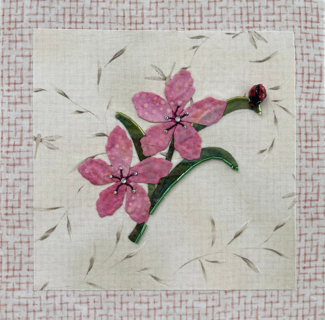8 x 8 fabric collage artwork featuring two pink flowers with crystal centers and a small ladybug detail made from inherited textiles