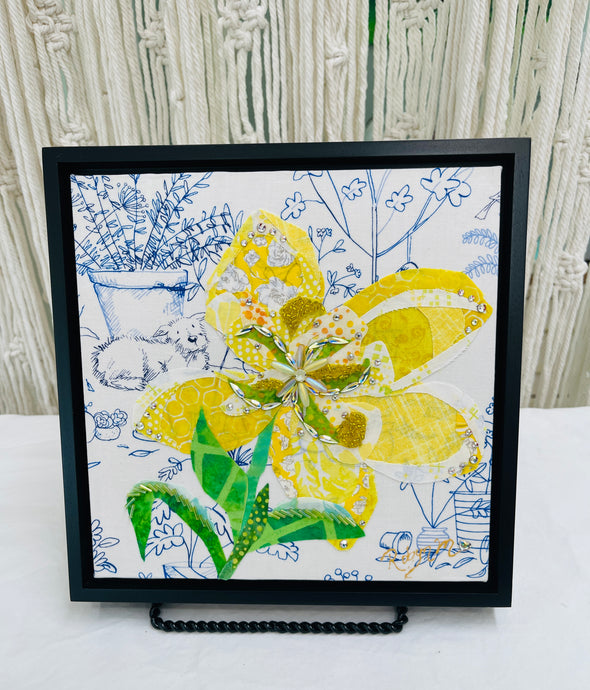 Yellow fabric flower artwork on 8x8 panel with layered textiles, Swarovski crystals, beads and green leaves on illustrated botanical background