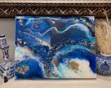 Abstract ocean artwork made with recycled glass and resin on a blue painted background, featuring textured waves and reflective details
